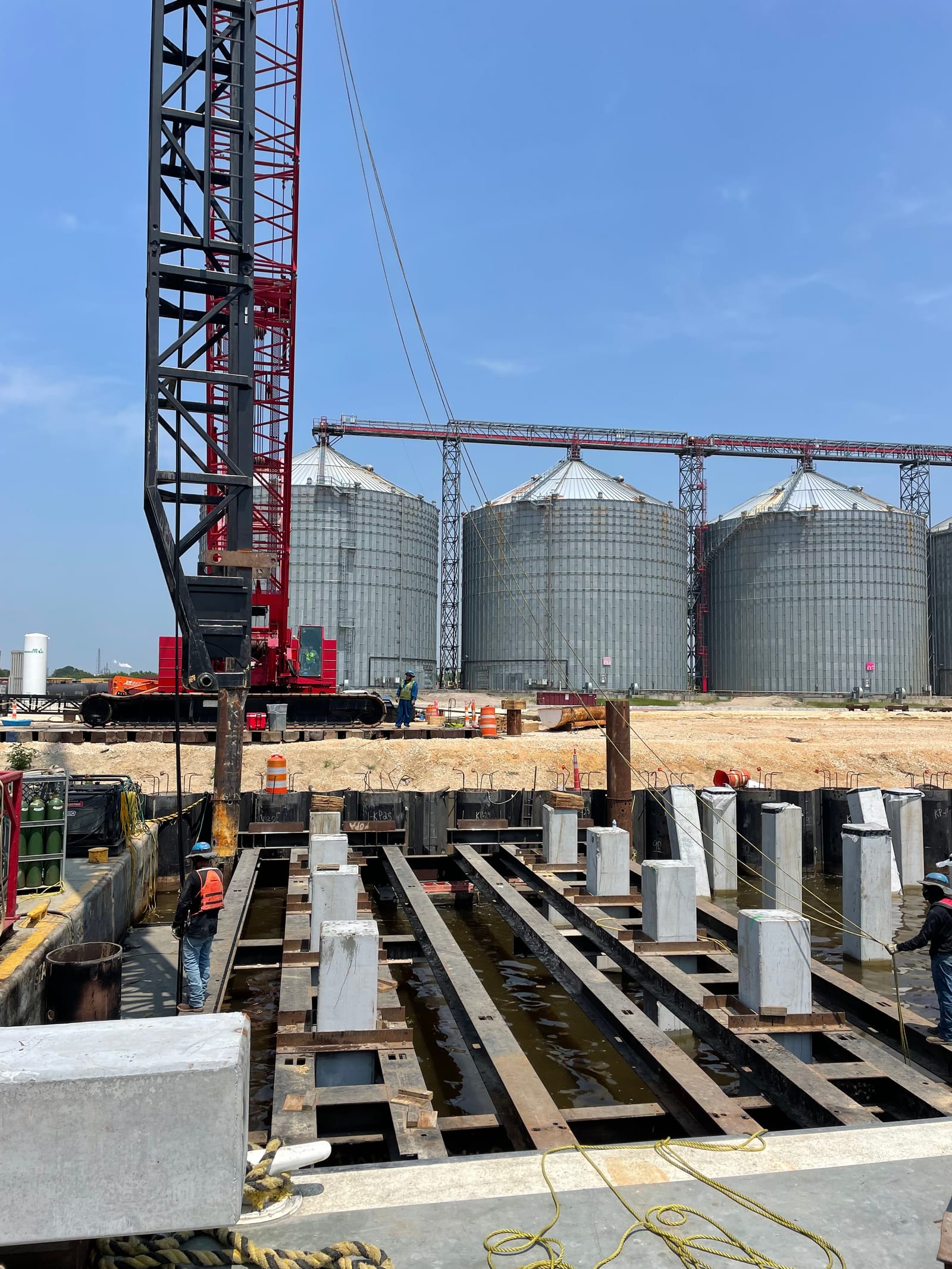 Construction management on an active jobsite — crane setting precast concrete elements near grain silos