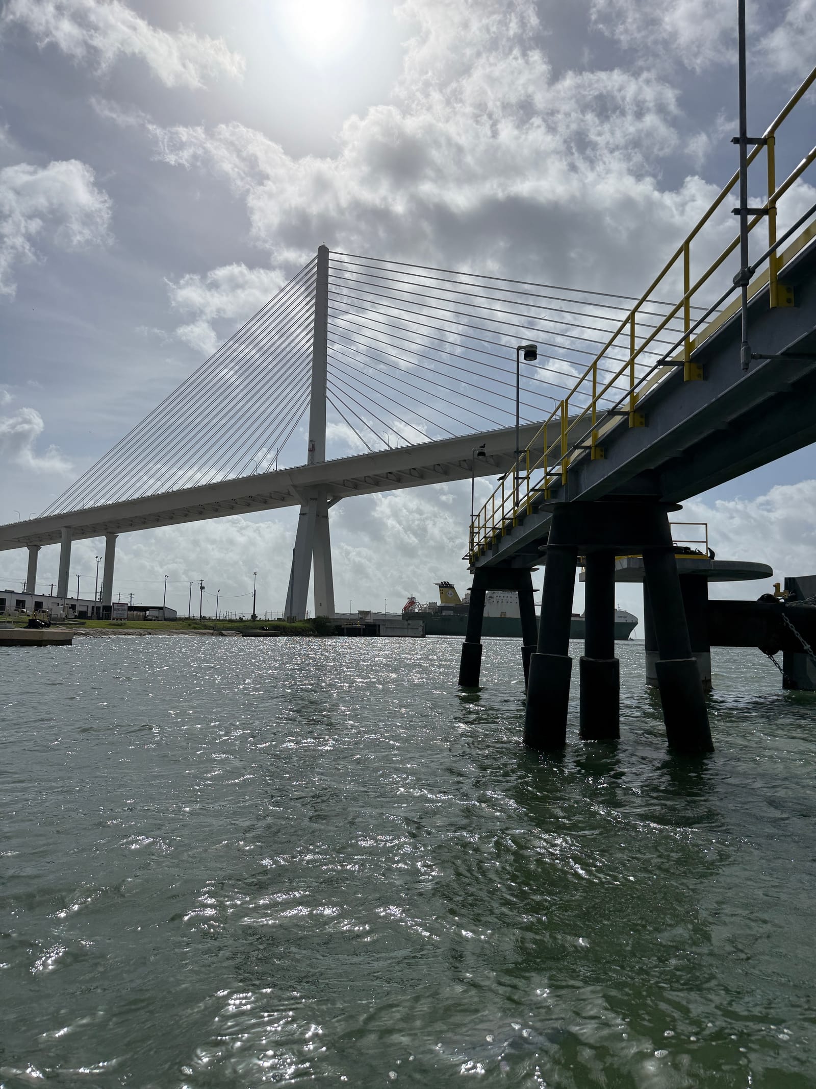 Marine pier on tubular steel pile bents over a port channel, with a cable-stayed bridge beyond